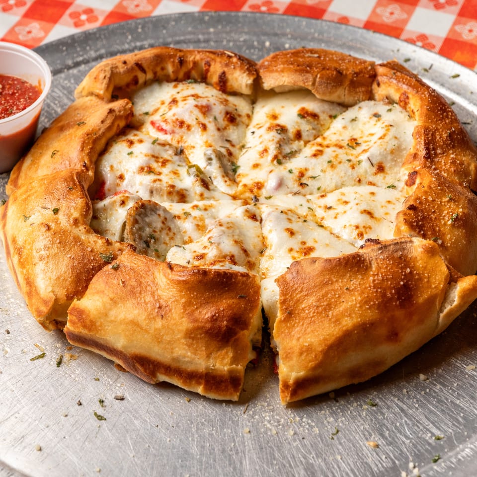 A golden-crusted calzone filled with melted cheese and sausage, served with a side of marinara sauce.