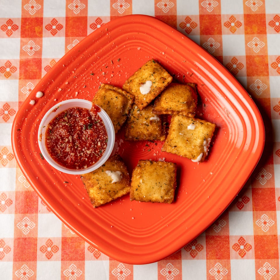 Fried ravioli with marinara sauce on a bright orange plate over an orange and white checkered tablecloth.