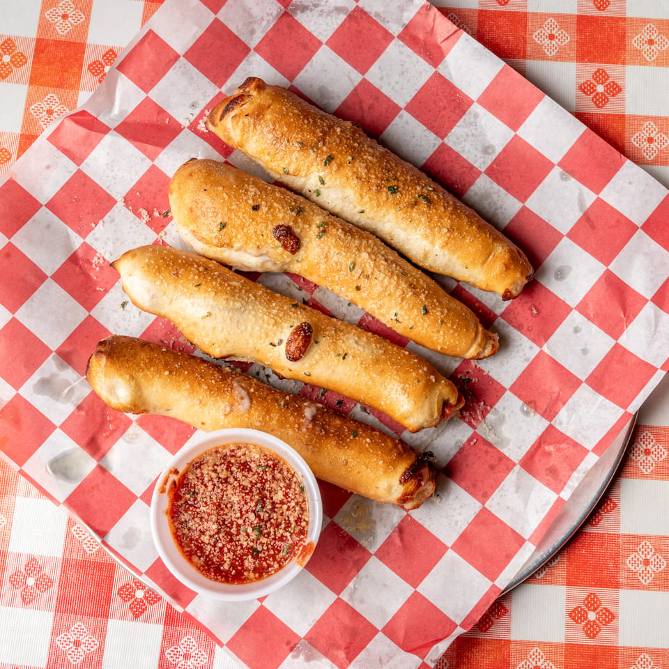 Four golden-brown pepperoni rolls with herbs and cheese, served with a side of marinara sauce.