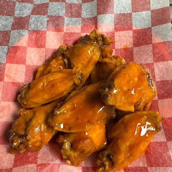 A close-up of several golden-brown chicken wings coated in a glossy orange sauce on red and white checkered paper.
