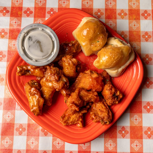 Buffalo wings with ranch dip and garlic knots on a red plate, on an orange and white checkered tablecloth.
