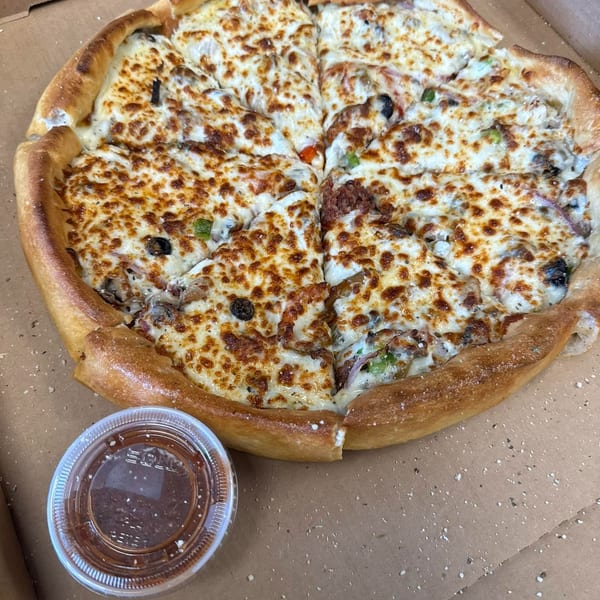 A freshly baked, sliced pizza with melted cheese and various toppings, alongside a dipping sauce.