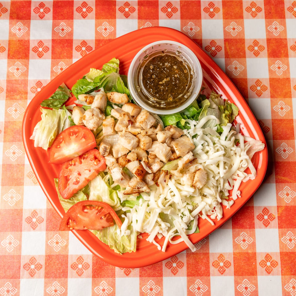 Chicken salad with lettuce, tomatoes, shredded cheese, and dressing on an orange plate.